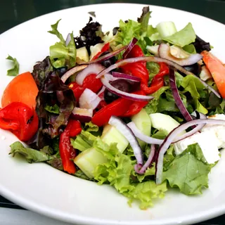 A mixed green salad with tomato, cucumber and red onion